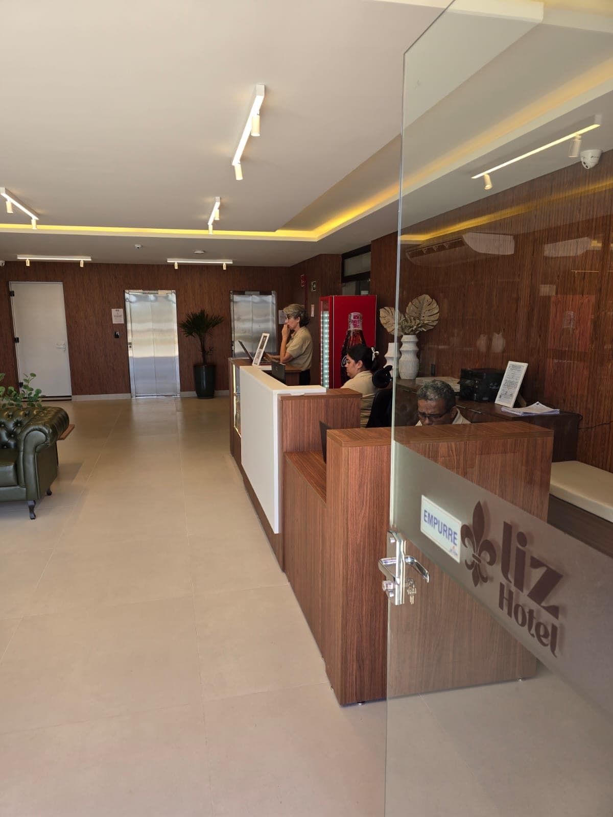 Recepção do Liz Hotel com balcão em madeira e equipe pronta para atender